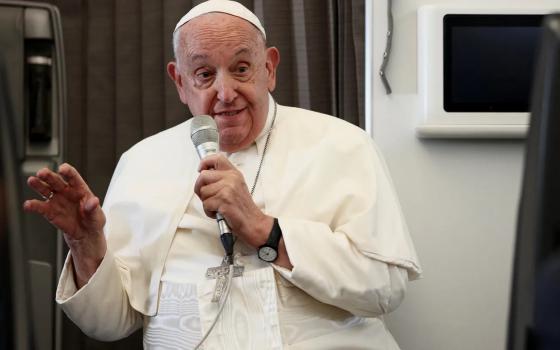 Francis sits, speaking into microphone and smiling. 