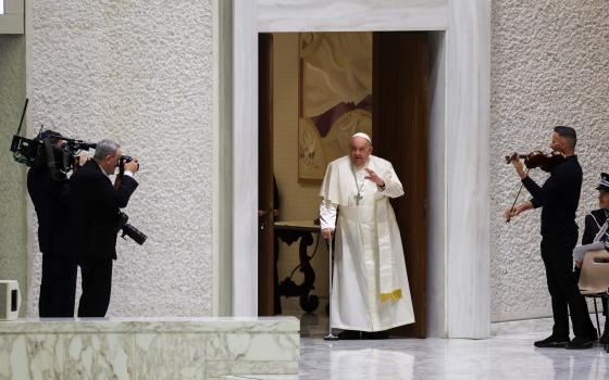 The pope enters room alone using cane.