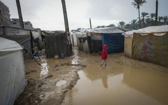 A young girl walks through a flooded street following overnight rainfall at the refugee tent camp for displaced Palestinians in Deir al-Balah, central Gaza Strip, Dec. 31, 2024. (AP/Abdel Kareem Hana)