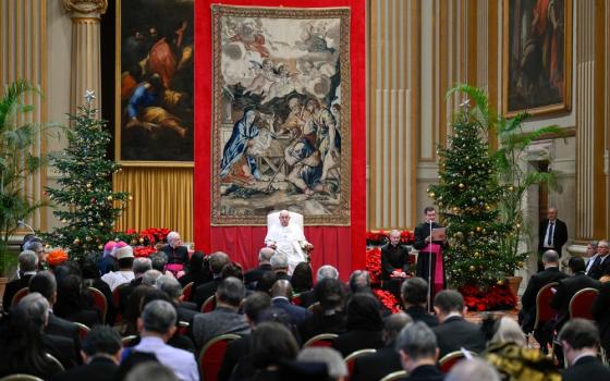 Pope sits on raised dais in front of tapestry facing diplomats.