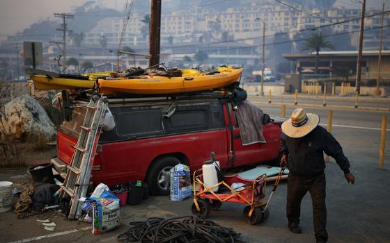 A man collects water along the Pacific Coast Highway, as powerful winds fueling devastating wildfires in the Los Angeles area force people to evacuate, in the Pacific Palisades neighborhood on the west side of LA on Jan. 8. Several Catholic parishes opened their doors to families evacuated from their homes as wind-driven fires continued to burn through parts of Los Angeles County Jan. 8. (OSV News/Reuters/Daniel Cole)