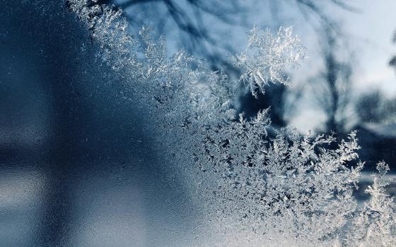 A closeup photo illustration shows frost and snowflakes against glass. (Unsplash/Sydney Rae)