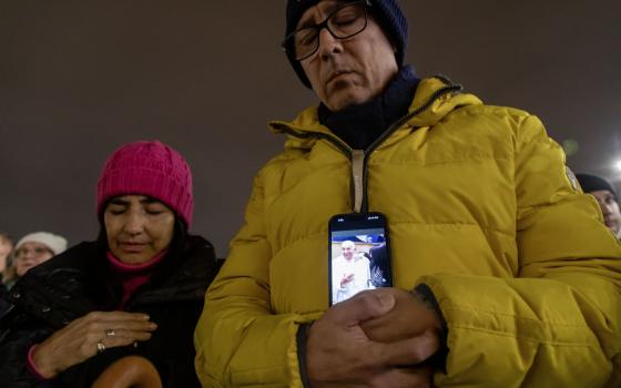 A man holds his phone displaying an image of Pope Francis as he joins Cardinal Pietro Parolin, Vatican secretary of state, in reciting the rosary for the pope in St. Peter's Square at the Vatican Feb. 24, 2025. Cardinals living in Rome, leaders of the Roman Curia and the faithful joined the nighttime prayer. (CNS photo/Pablo Esparza) 