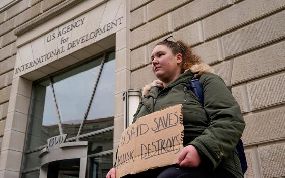 A woman holds a placard outside the U.S. Agency for International Development building in Washington as it sits closed to employees Feb. 3, 2025, after a memo was issued advising agency personnel to work remotely. (OSV News/Reuters/Kent Nishimura)