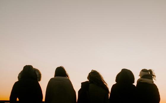 A group of people, backs turned, face toward a foggy horizon in an outdoor setting.  (Unsplash/Annie Williams)