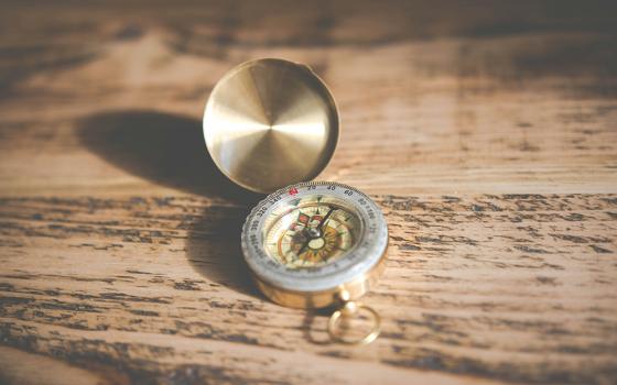 A golden compass on a wooden table (Unsplash/Chris Lawton)