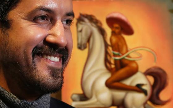 Mexican artist Fabian Chairez stands next to his painting showing Mexican Revolution hero Emiliano Zapata straddling on a horse nude, wearing high heels and a pink, broad-brimmed, during an interview at the Fine Arts Palace in Mexico City, Wednesday, Dec. 11, 2019.