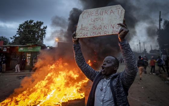 A supporter of presidential candidate Raila Odinga holds a placard referring to electoral commission chairman Wafula Chebukati, while shouting "No Raila, no peace", next to a roadblock of burning tires Aug. 15 in Nairobi, Kenya. (AP photo/Ben Curtis)